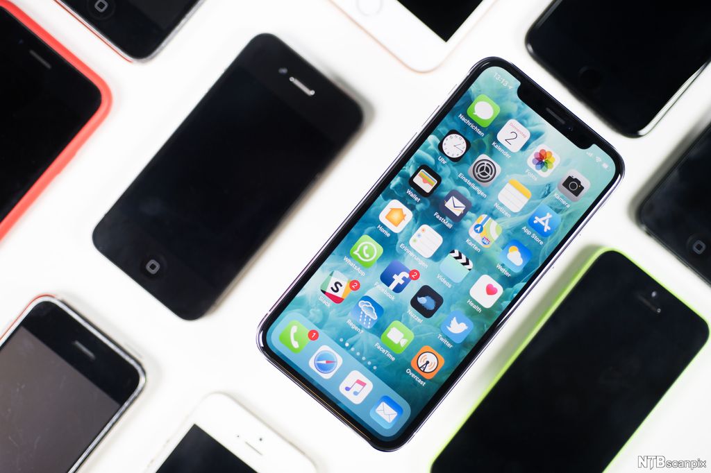 En iPhone X ligger på et bord ved siden av andre modeller. Illustrasjon.