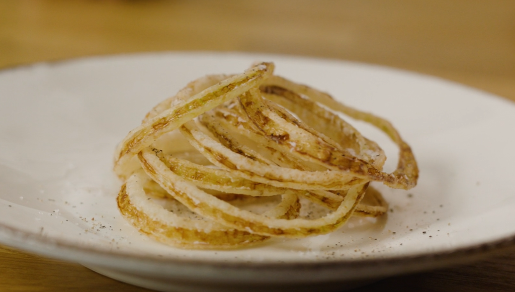 Friterte løkskiver anrettet på en hvit tallerken. Foto.