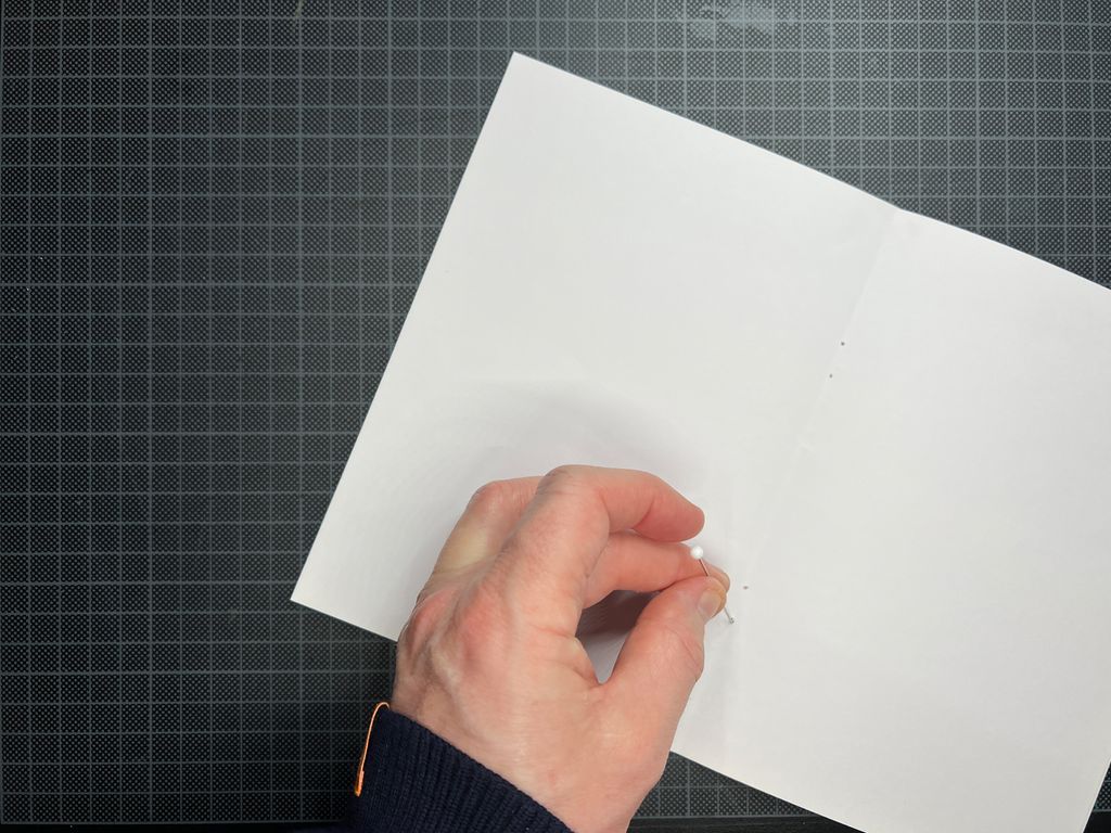 Ei hånd stikker hull i et ark. Foto.