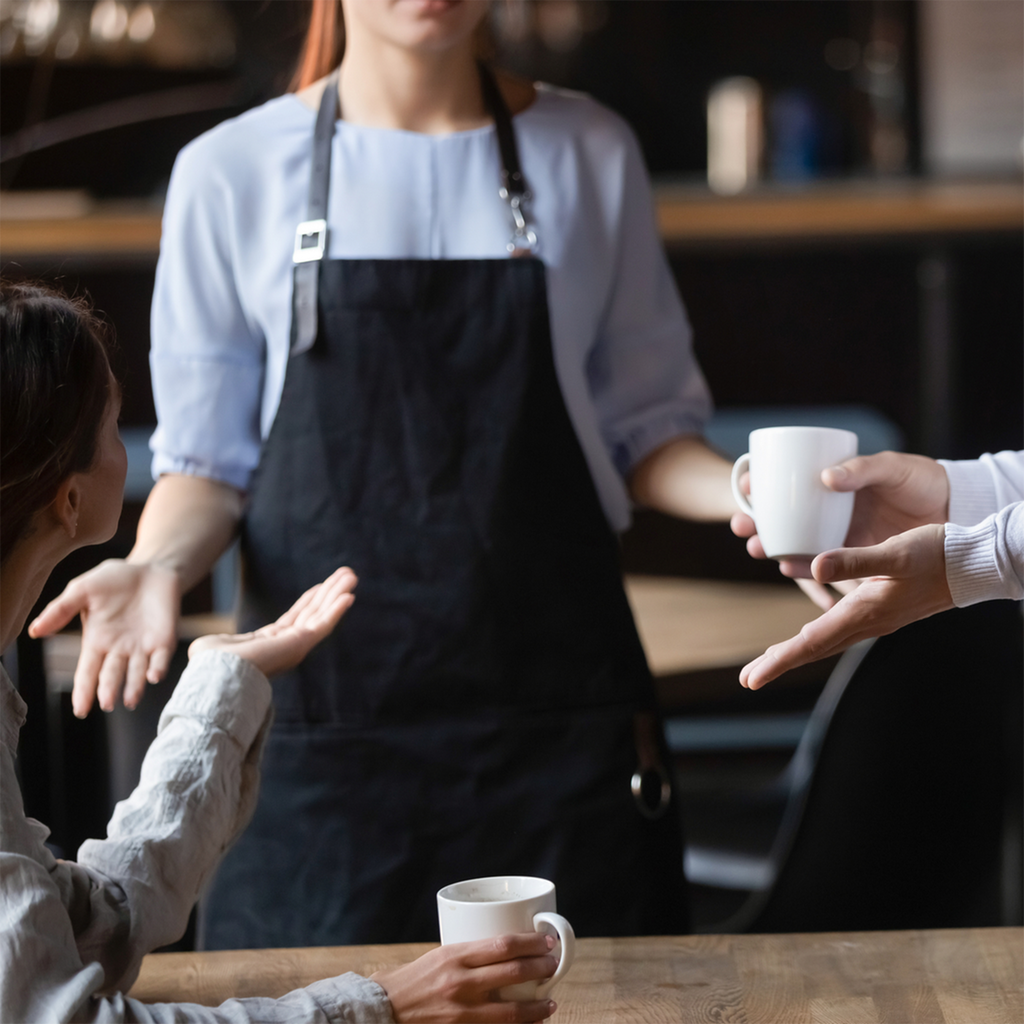 To gjester i ein kafé diskuterer med ein servitør. Dei gestikulerer. Foto.