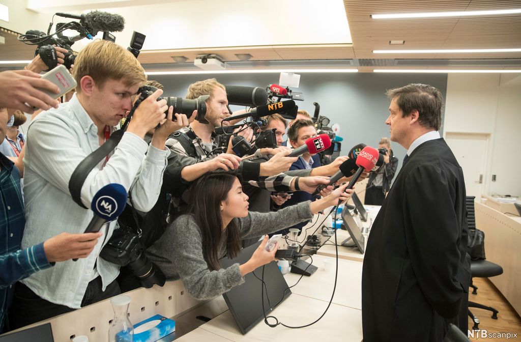 Advokat intervjues av en flokk journalister i en rettssal. Foto.