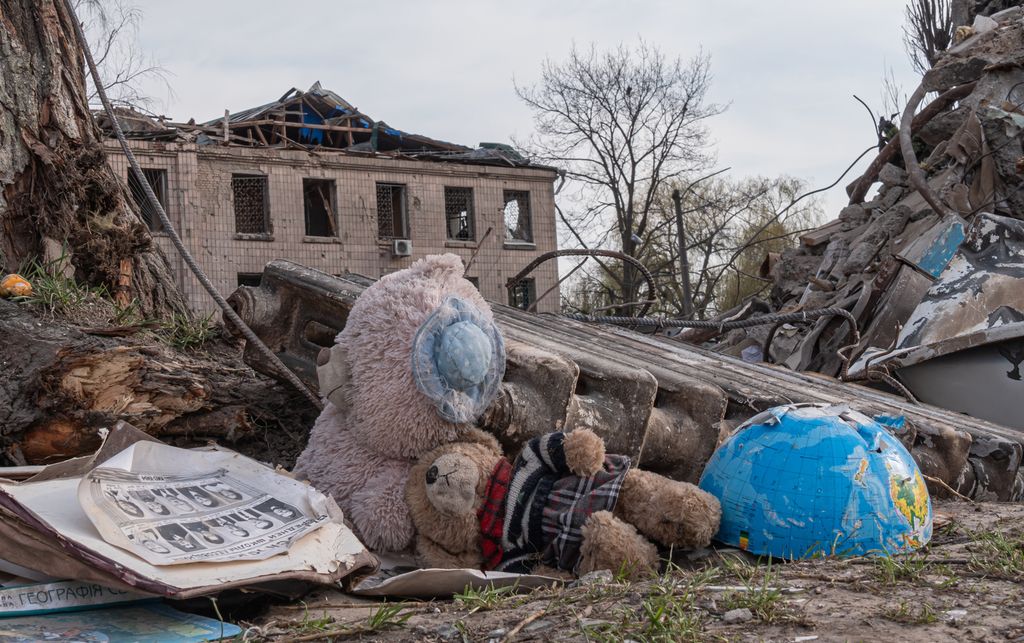 Buildings destroyed by bombs. In the foreground we see two teddy bears and half a globe. Photo.