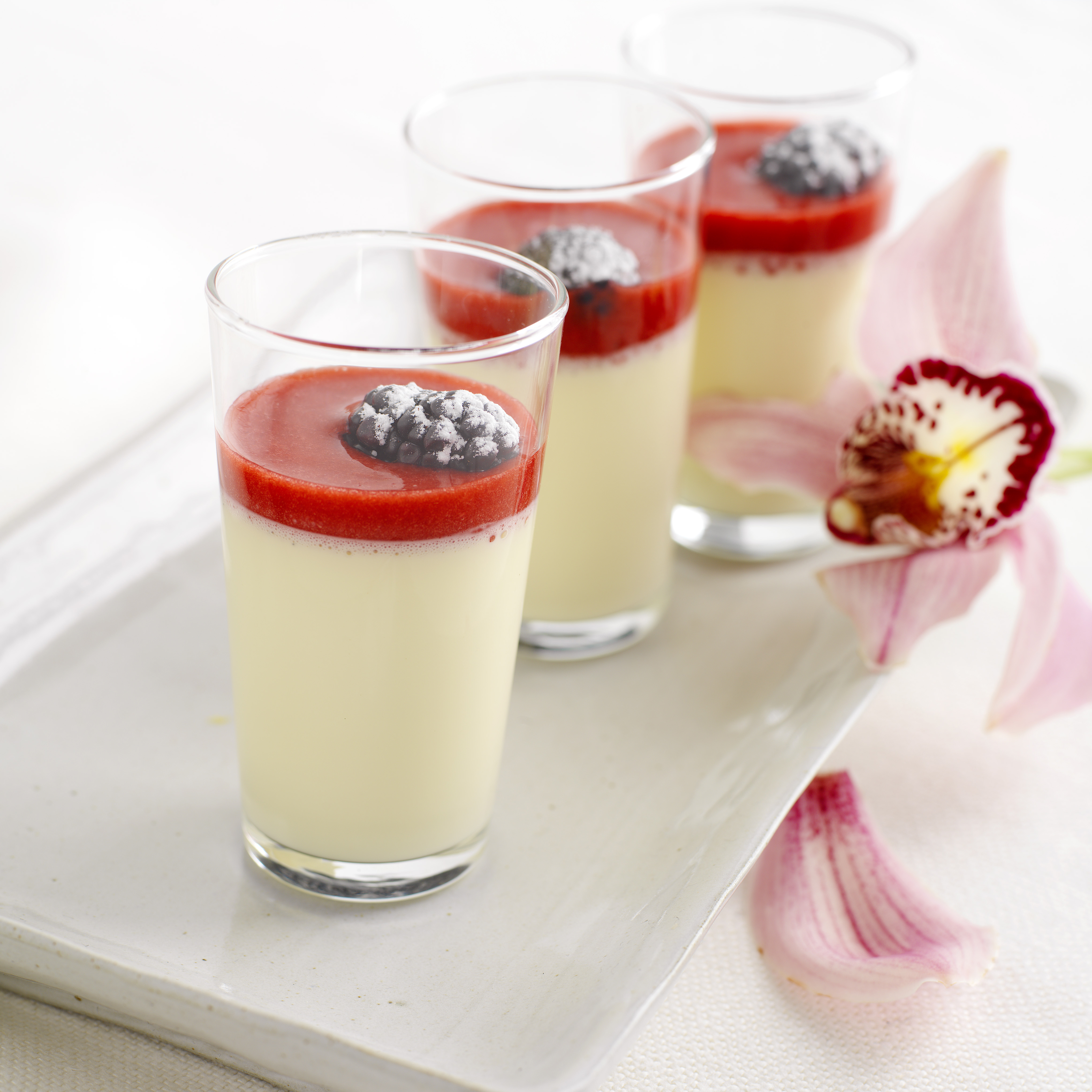 Høye glass med hvit pudding og rød bærsaus på toppen. Foto.