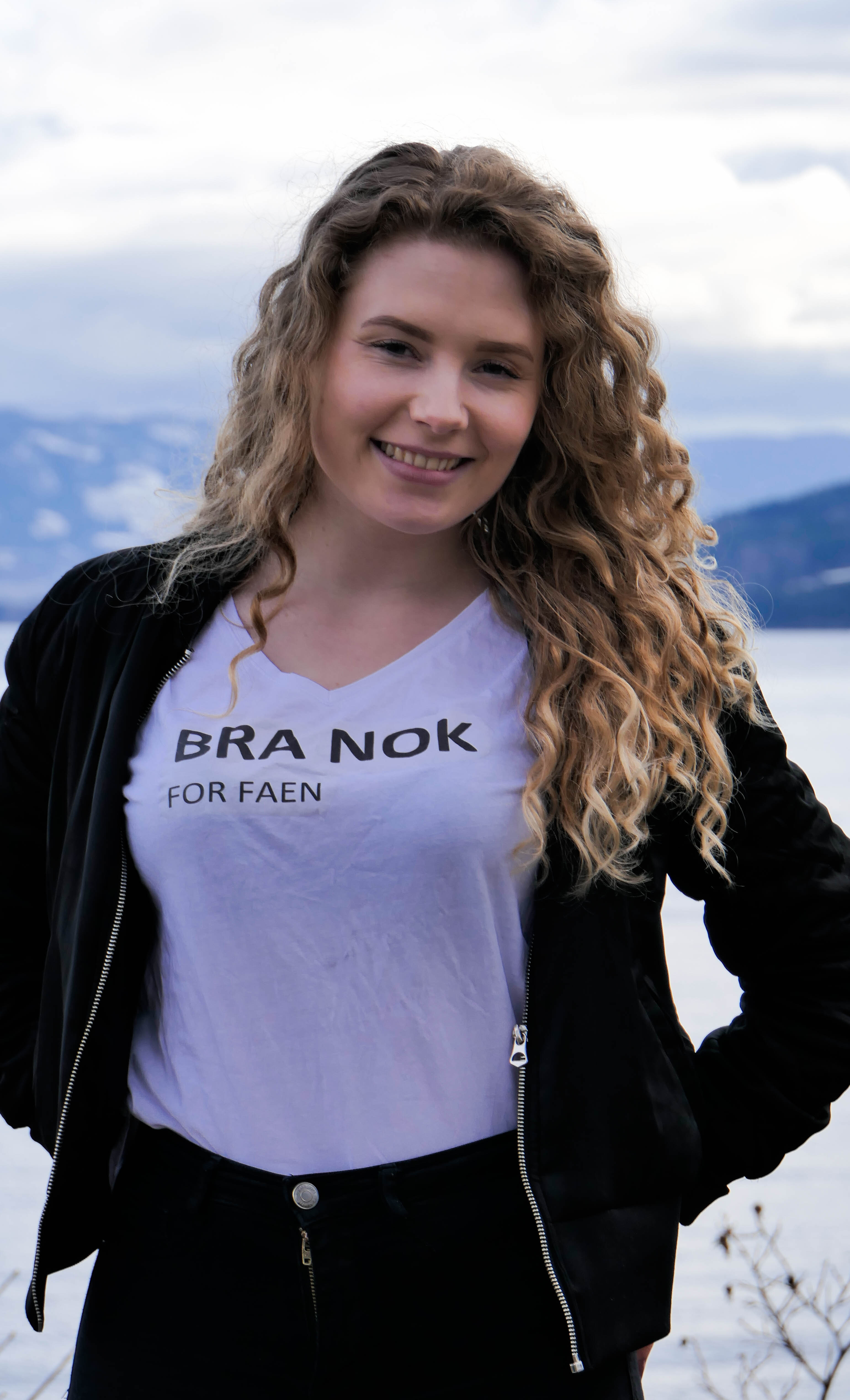 En ung kvinne poserer for kamera med en T-skjorte der det står "Bra nok – for faen". Foto.