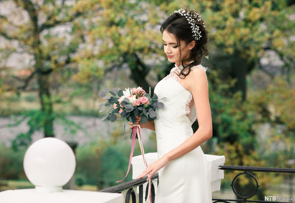 Vakker brud som ser på blomsterbuketten sin. Foto.