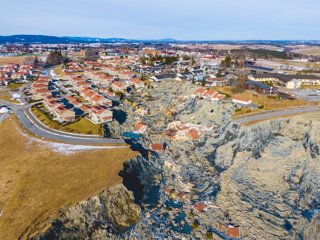 Svær rasgrop som dekker deler av et boligområde, en vei og et jorde. Flere hus har havnet i rasgropa, mens andre hus balanserer på kanten av rasgropa. Foto.