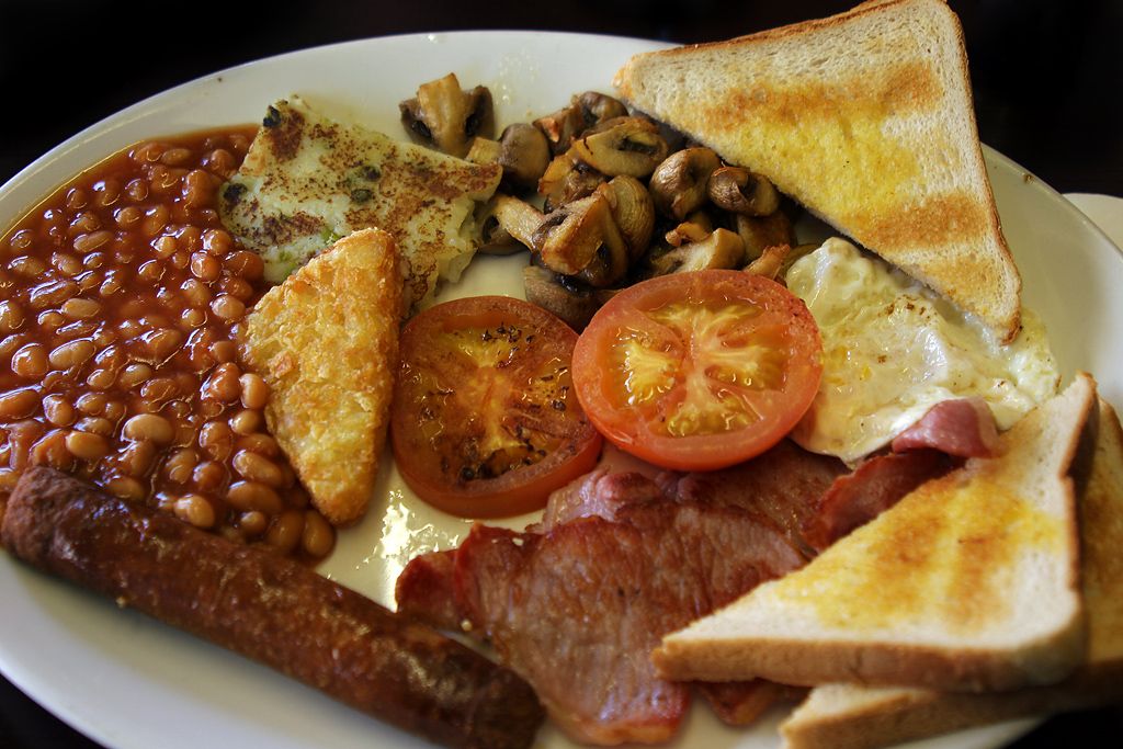 En engelsk frokosttallerken med stekte egg, bacon, blodpølse, toast, stekt sopp, tomat og tomatbønner. Foto.