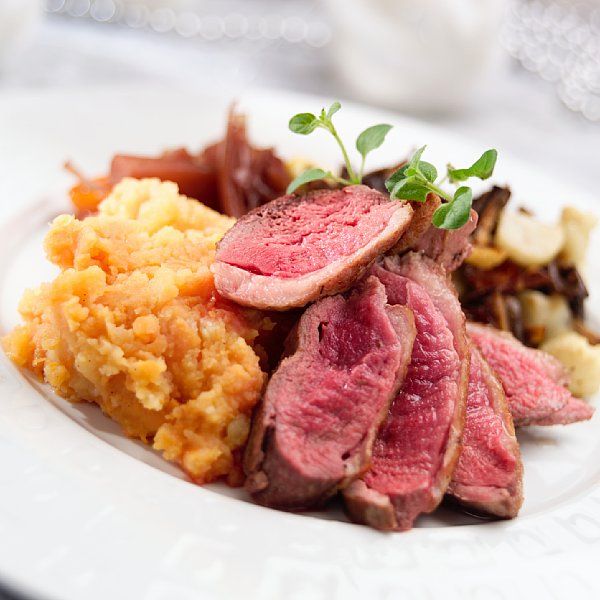 Saftige kjøttstykker og gul potetmos anrettet på hvit tallerken. Grønne blader er brukt som garnityr. Foto.