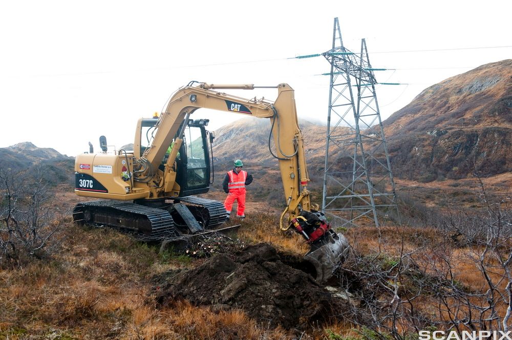 Gravemaskin som graver i fjellandsskap for å sette ned kraftmast. Foto.