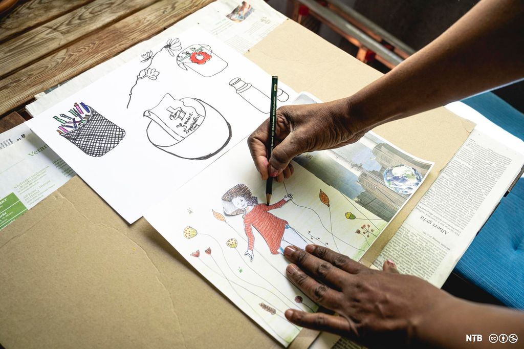 Hender som tegner en tegning med mange figurer. Foto. 