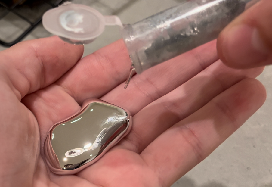 Hånd med flytende og sølvglinsende metall. Foto.