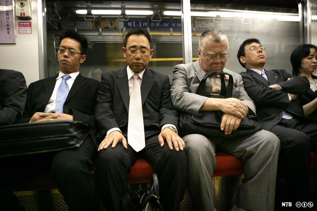Menn med dress og slips som sover mens de kjører T-bane i Tokyo. Foto. 