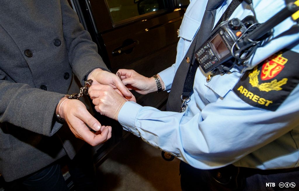 Politiet i arbeid. En politibetjent i uniform låser håndjern på en person. Hodene er ikke synlige. Foto.
