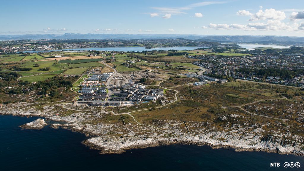 Flyfoto av et boligfelt som ikke ligger så langt fra havet. I bakgrunnen er det landbruksområder til venstre og mer tettbygde strøk til høyre. Foto.