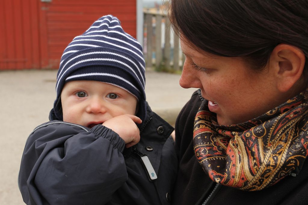 En kvinne holder et lite barn med parkdress på. Foto.