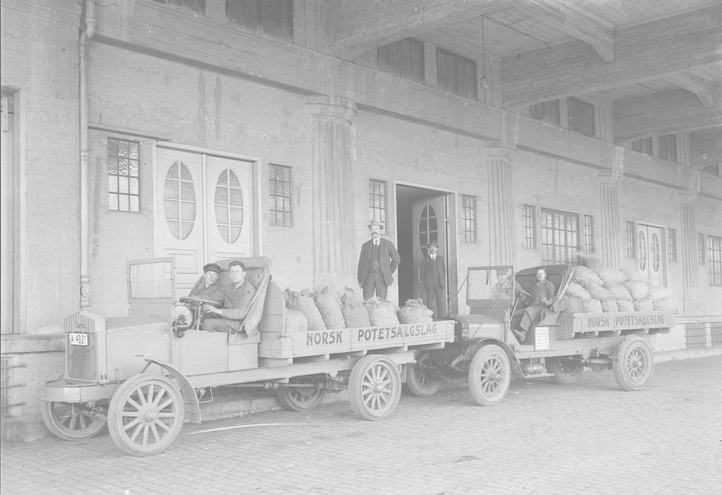 Historisk svart-hvitt bilde av biler med påskriften Norsk potetsalgslag og potetsekker på lasteplanene. Foto.