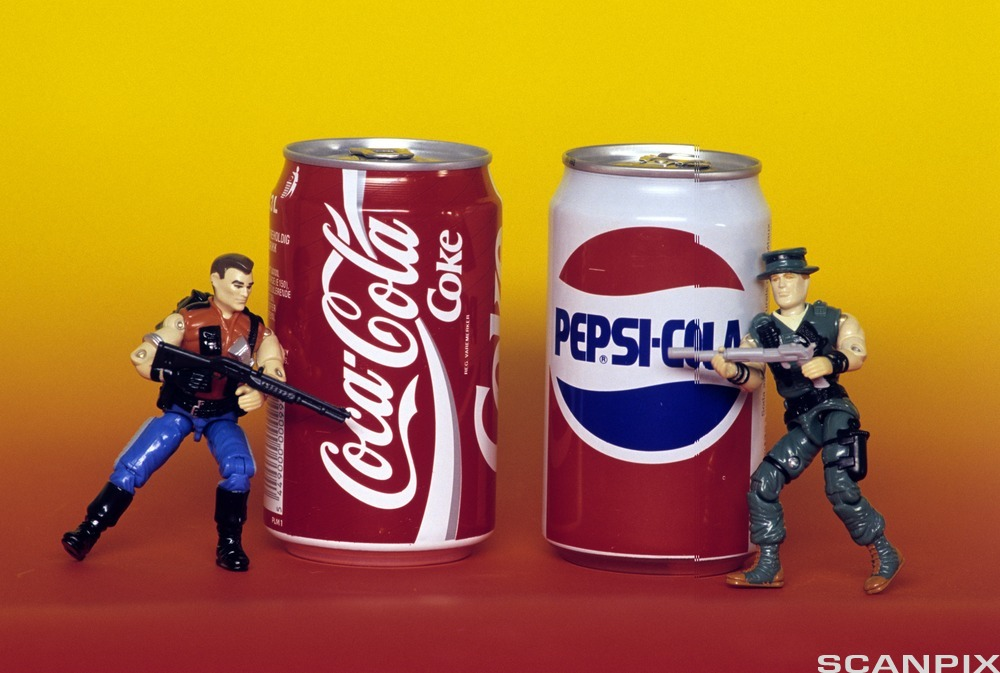 En colaboks og en pepsiboks med hver sin actionfigur ved siden av. Figurene peker på hverandre med skytevåpen. Foto.