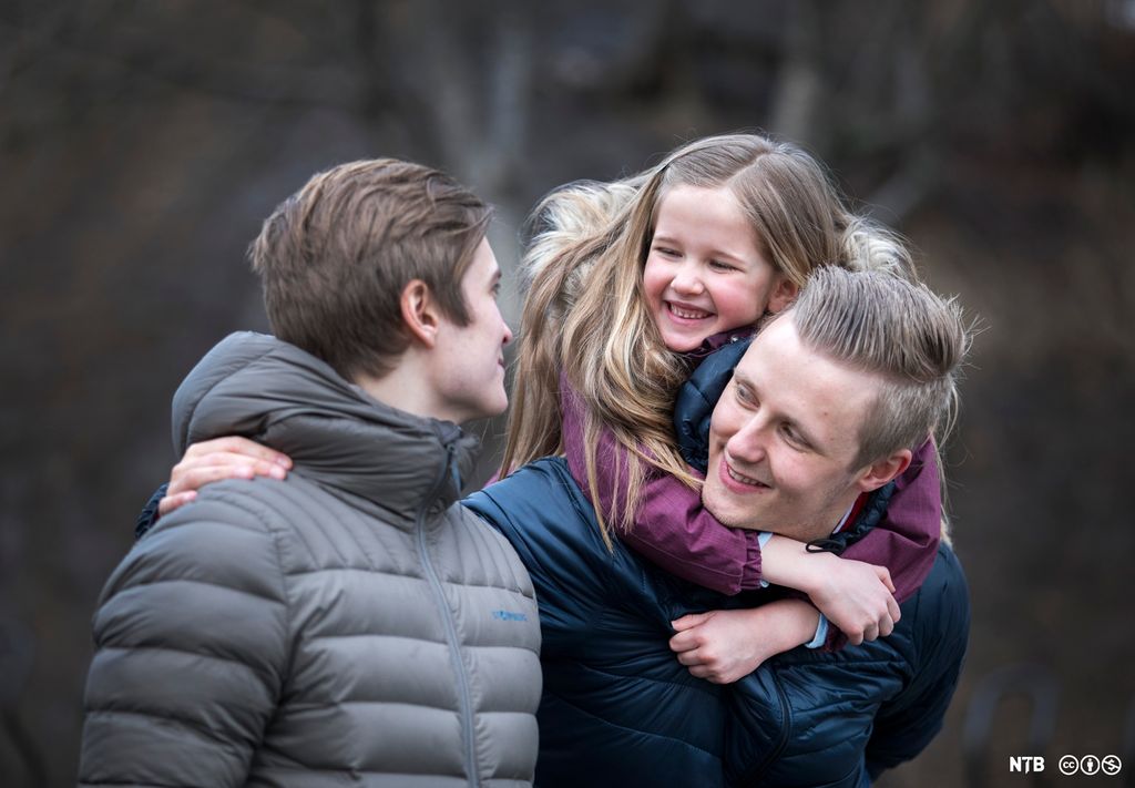 To storebrør saman med ei veslesøster. Veslesøstera sit på ryggen til den eine broren. Foto.