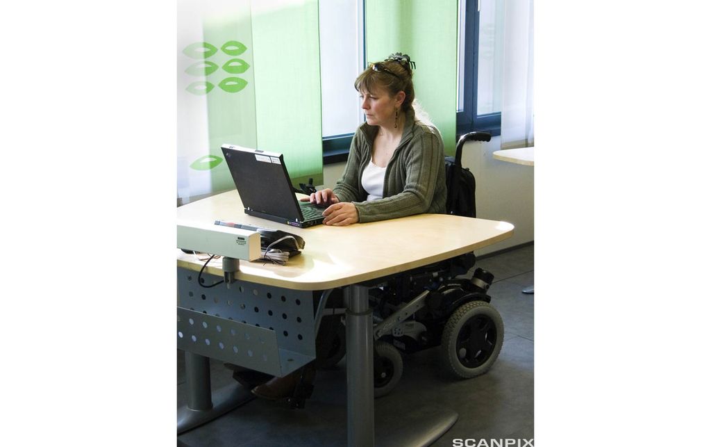 Kvinne i rullestol arbeider ved en kontorpult Foto.