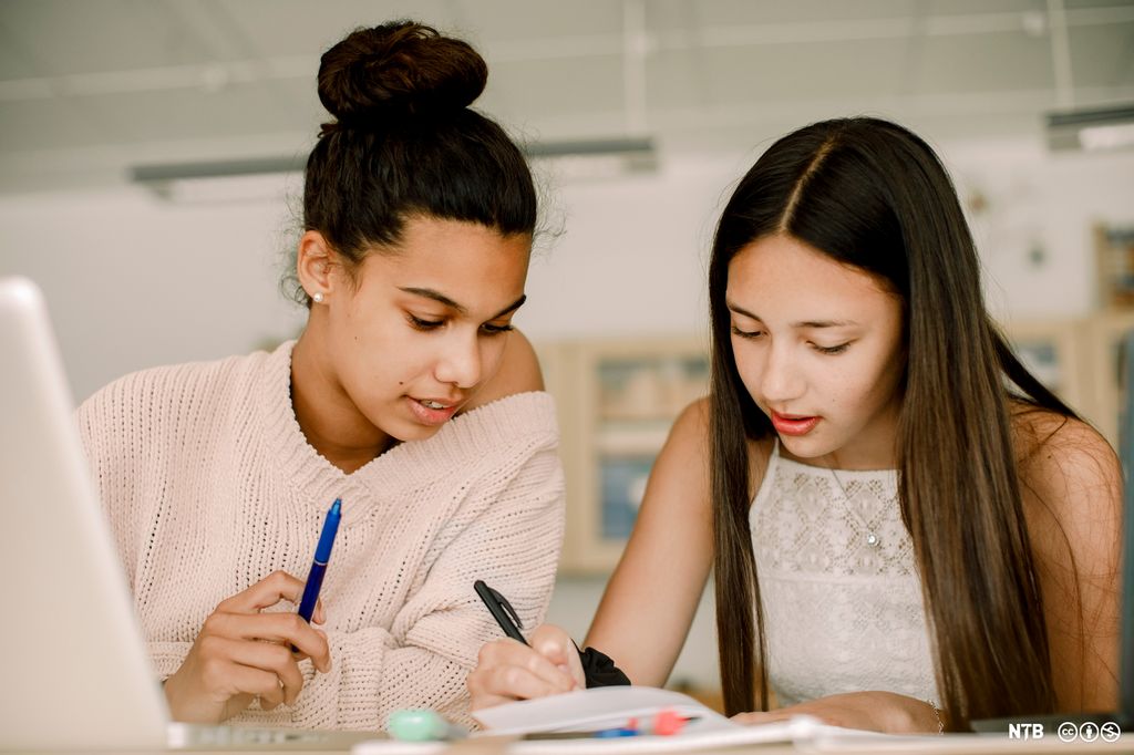 To jenter sitter ved en pult og samarbeider om notater. Foto.