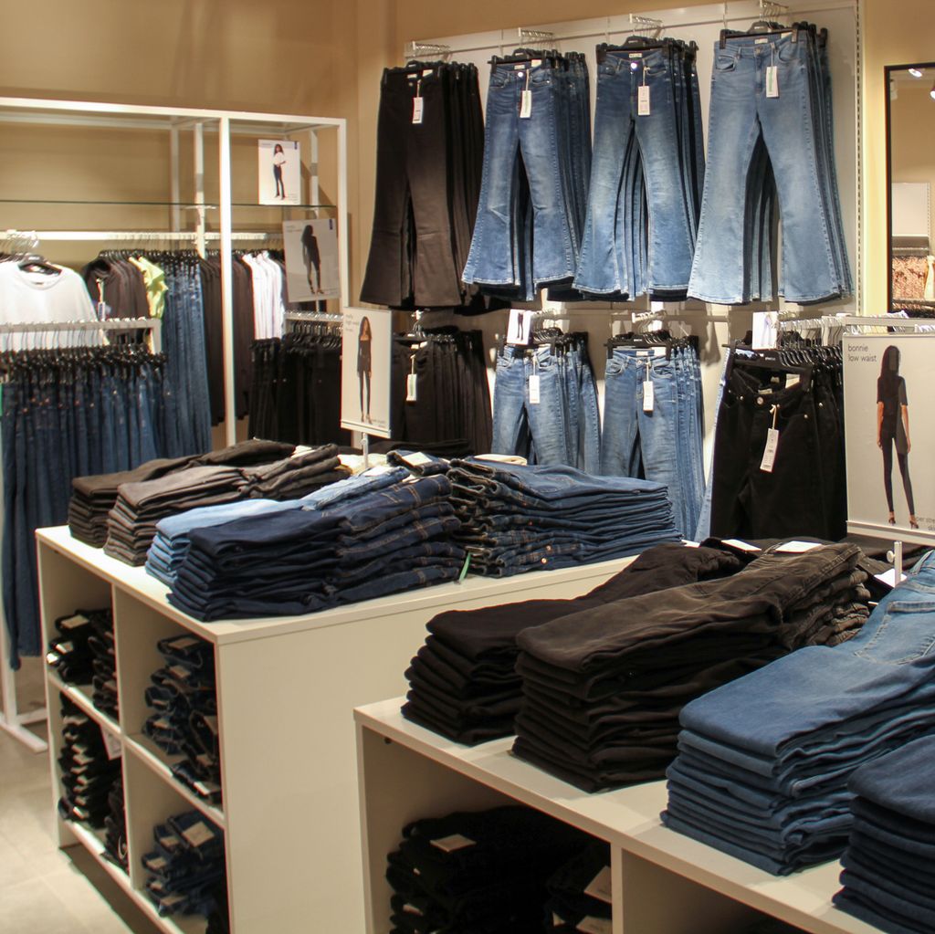 Utsnitt fra klesbutikk. Det henger bukser langs veggene, og det ligger pent sammenbrettede bukser på bord midt i rommet. Foto.