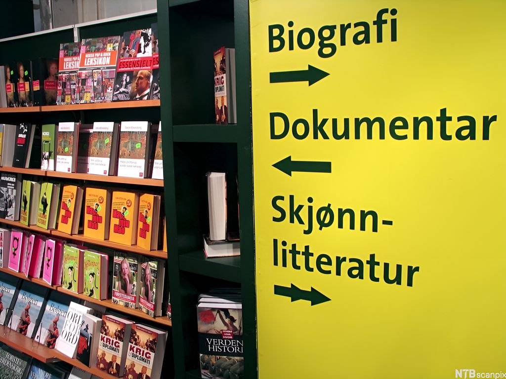 Bokhyller i bokhandel, og skilt som viser vei til biografier, dokumentarlitteratur og skjønnlitteratur. Foto.