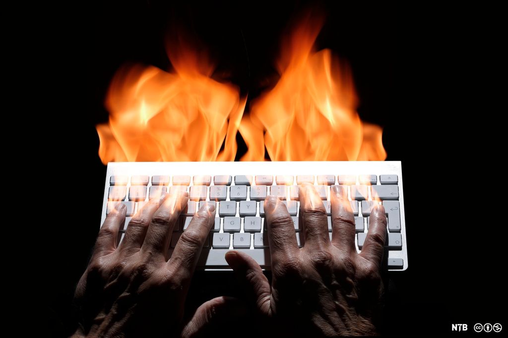 To hender skriver på et tastatur i et bekmørkt rom. Det står høye flammer opp av fingrene. Foto.