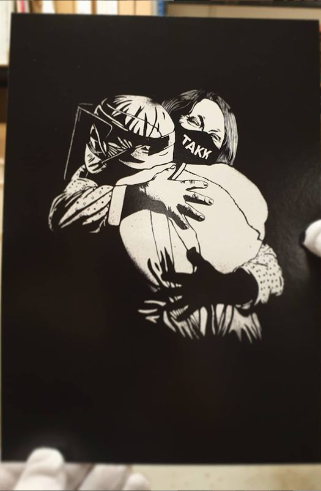 Kort med sjablongtrykk av en sykehusansatt i fullt verneutstyr som får klem av en pasient med munnbind påskrevet "TAKK". Foto.
