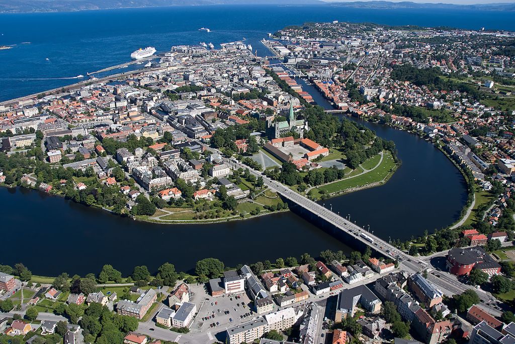 Trondheim sentrum sett fra lufta. Midtbyen, ei slags halvøy, er omrammet av fjorden og Nidelva. Flere broer går over elva. Nidarosdomen og Erkebispegården er cirka midt i bildet. I bakgrunnen, på fjorden, er det flere cruisebåter. Foto.