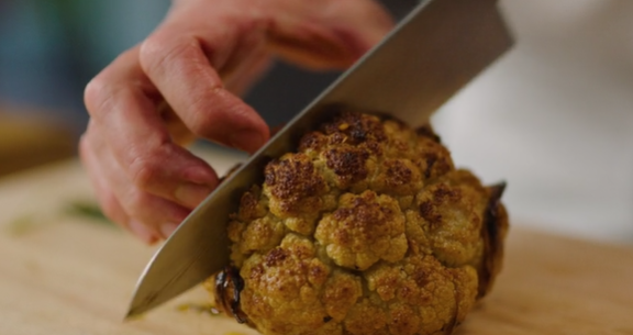 En helbakt blomkål deles i to med en kniv. Foto.