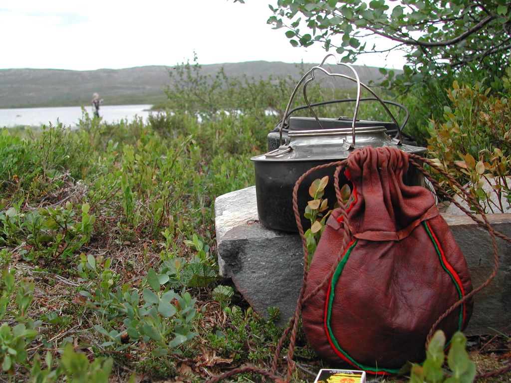 To kaffekjeler på en stor stein i skogen, med en skinnpose og en fyrstikkeske ved siden av. Foto.