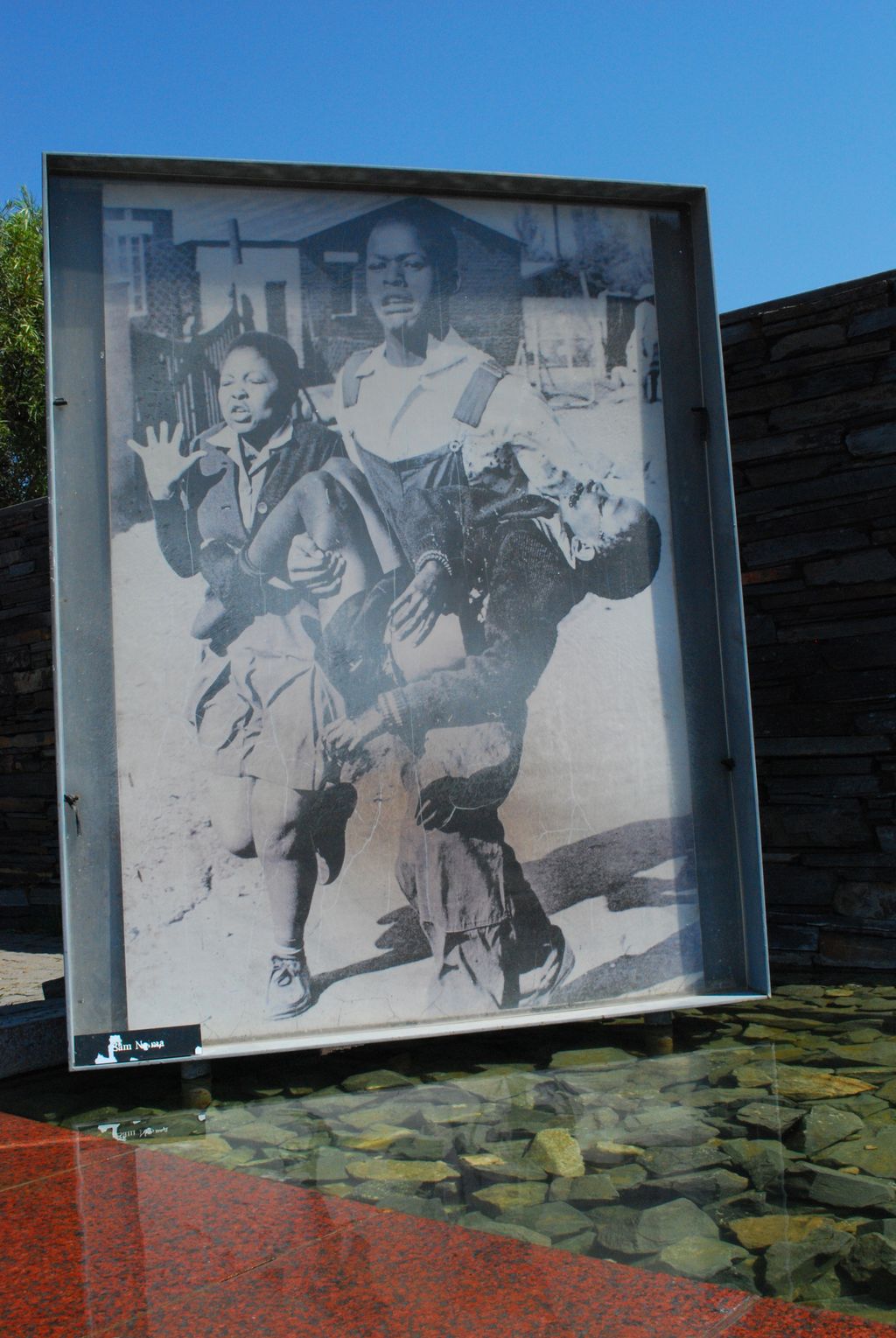 A man is carrying a wounded child. A woman is walking next to him. Black and white photo.