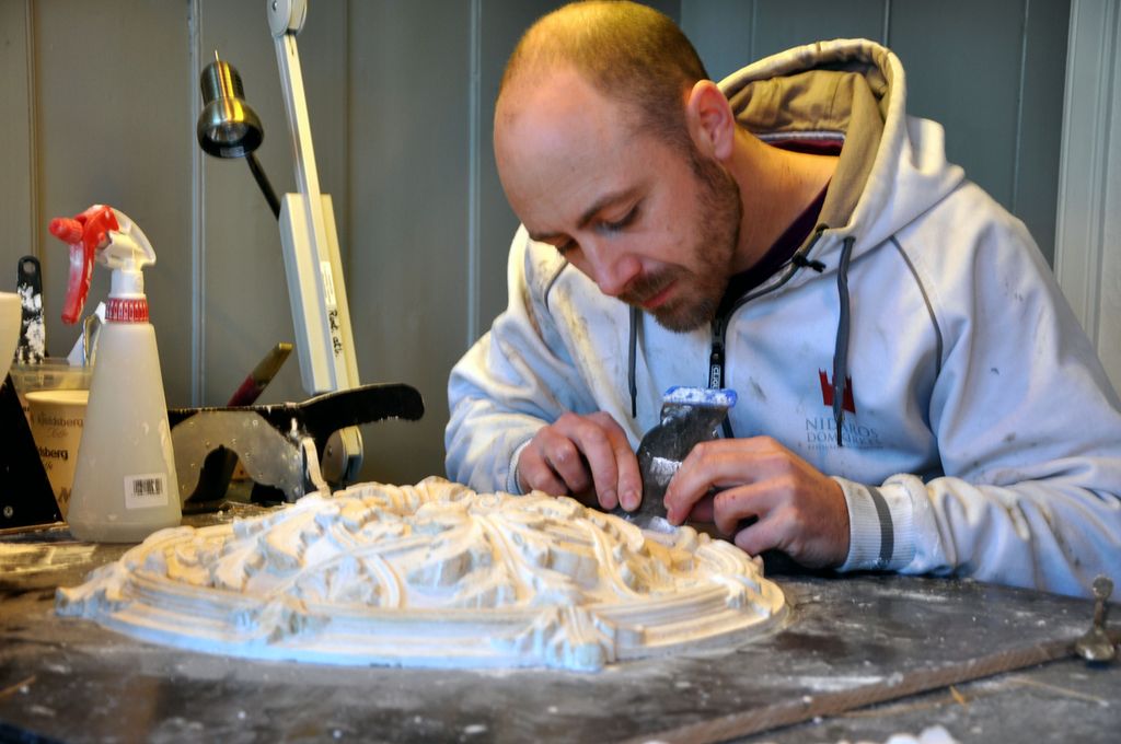 Gipsmaker som arbeider med en takrosett av gips. Foto.