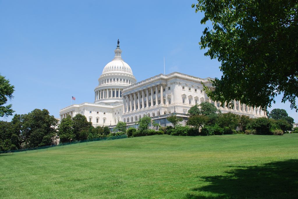 Photo: We see a large, white building in classical style. The building has columns and a large dome. The building is situated in or near a park. 
