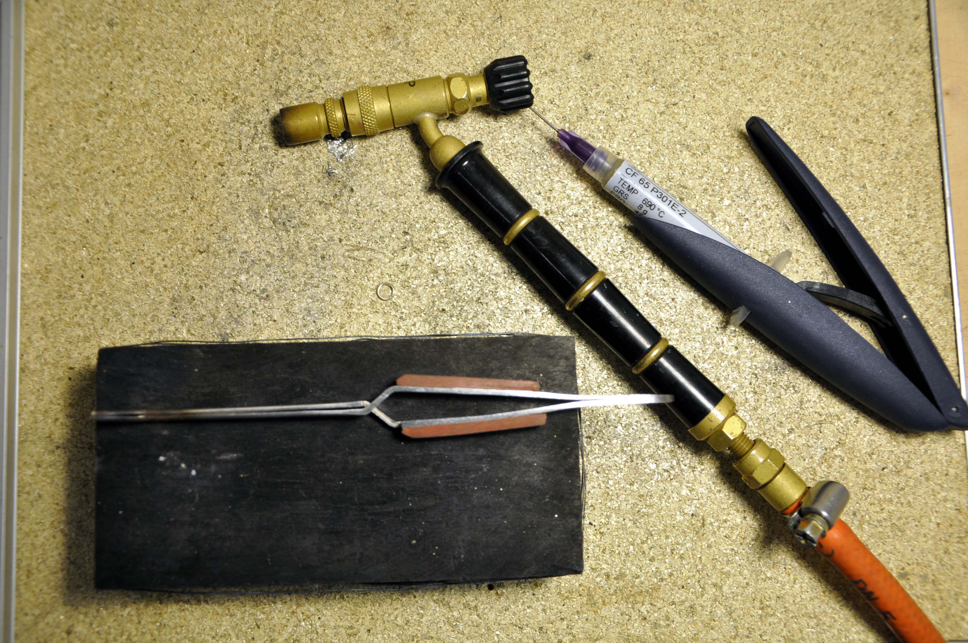 Loddetang, loddepistol, flussmiddel og slagglodd ligger utover et bord. Foto.