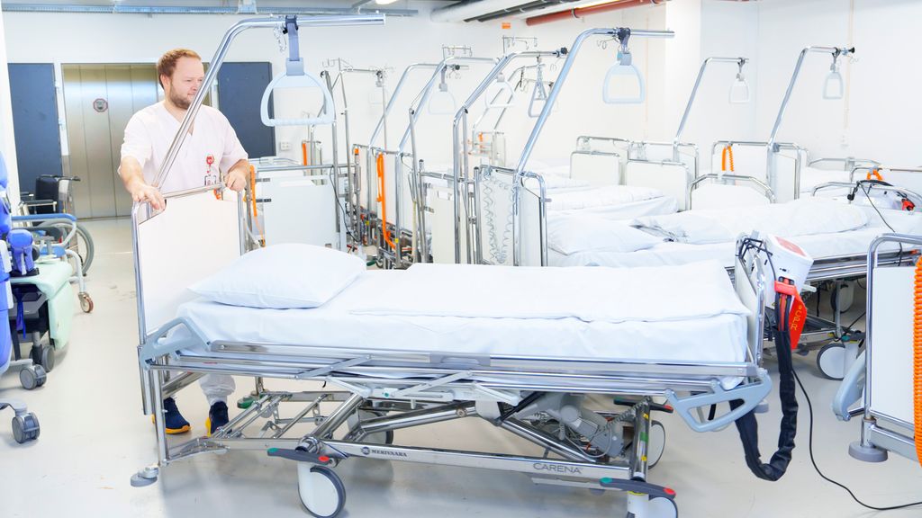 Person i uniform for helsepersonell organiserer rene senger på sengesentral. Foto.