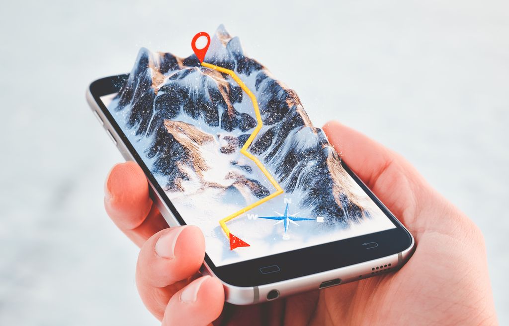Hånd som holder i en mobiltelefon. Fjell med en inntegnet reiserute stikker opp fra skjermen. Illustrasjon.