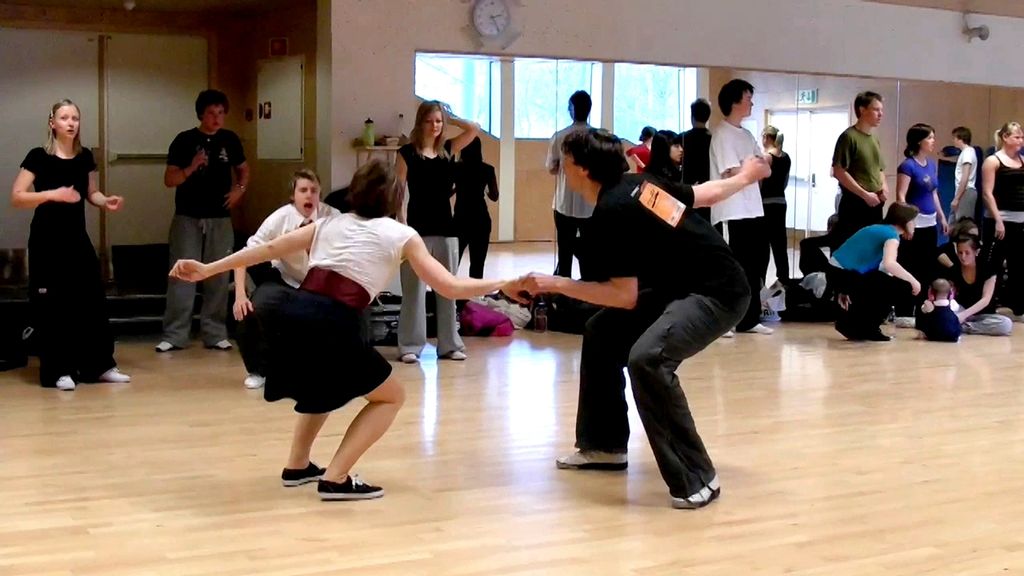 En mann og en kvinne danser i en gymsal. Flere ser på og heier på dem, andre er opptatt med andre ting. Foto.