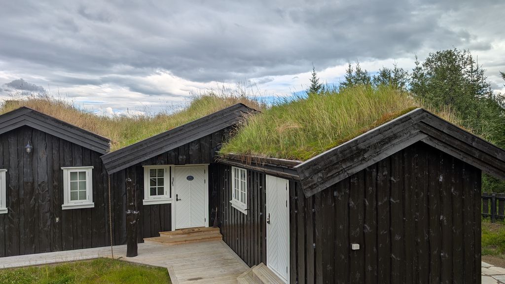 Hytte med torvtak. Ho har eit tilbygg der høgre side av taket fell saman med taket på resten av hytta. Fordi mønet på tilbygget ikkje går så høgt som mønet på resten av hytta, utgjer den høgre delen av taket på tilbygget ei eiga flate. Foto.