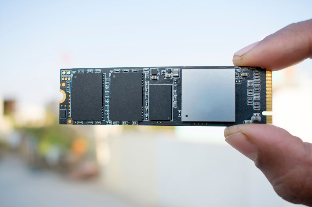 To fingre holder et lite, avlangt kretskort med fire mikrobrikker. To av mikrobrikkene er for lagring, én for buffer og én for kontroller. Foto.