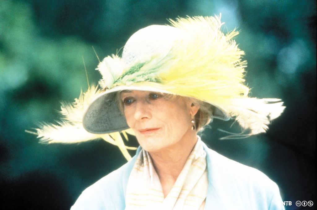 Photo: An older woman, wearing a big hat with photos on it. 
