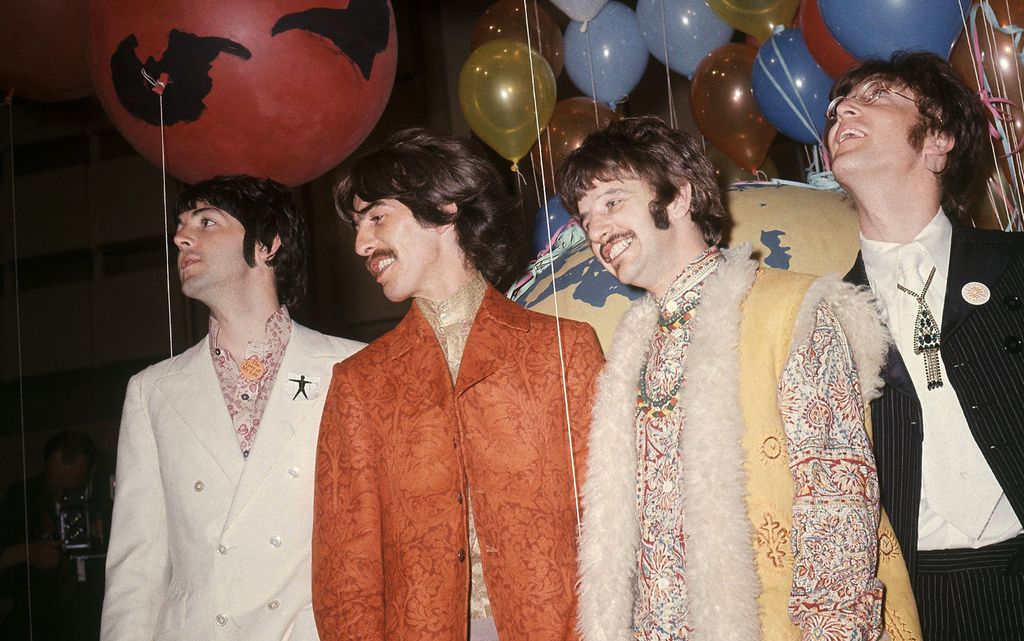 Gruppa The Beatles. Paul McCartney har hvit dobbelspent dress med rosamønstrete skjorte, George Harrison har gullskjorte og en oransje dressjakke med brokademønster, Ringo Starr har skjorte med fargerikt mønster og en vest med hvit pelskant, John Lennon har en klassisk mørk tynnstripete dress og et smykke med stort anheng som henger utenpå slipset. Foto.