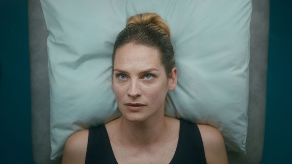 Kvinne med alvorlig ansiktsuttrykk hviler hodet på ei pute og ser rett opp. Foto.