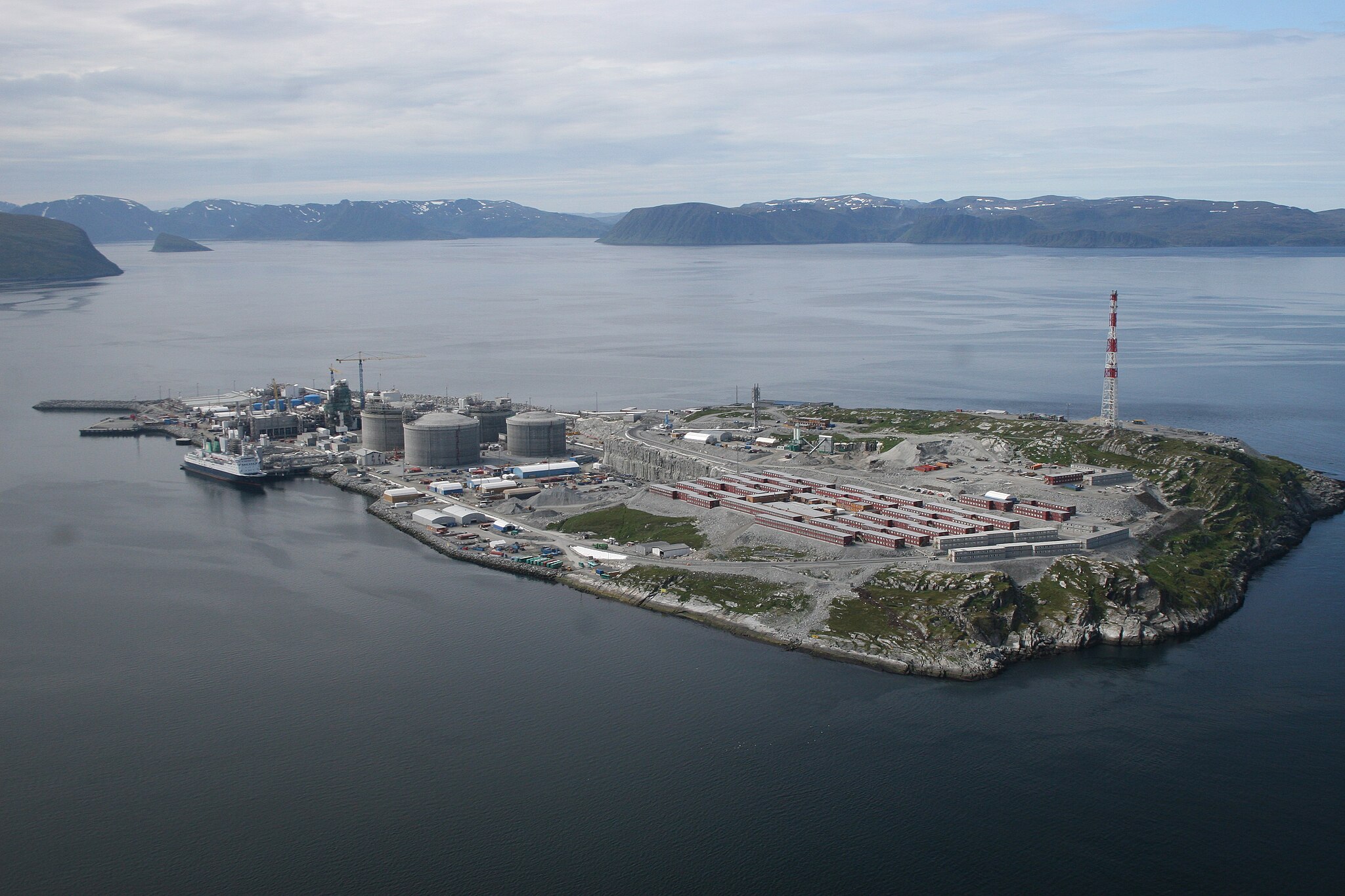 Øy som mer eller mindre er dekket av industriinstallasjoner, som tanker, konteinere og kraner. Et skip ligger til havn. Foto. 