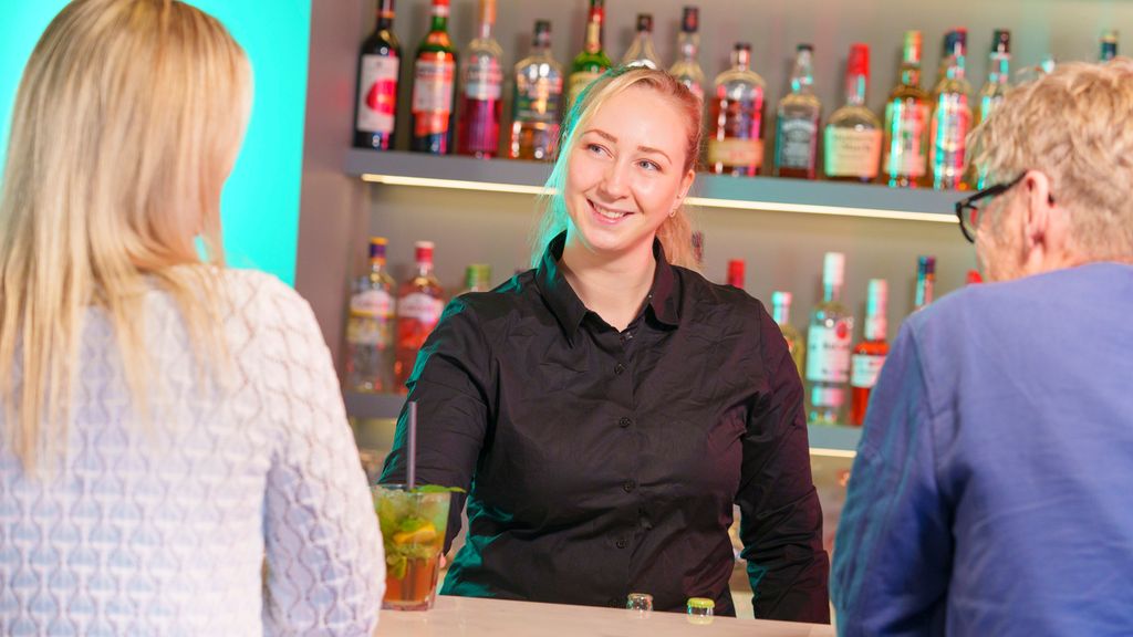 Smilende bartender serverer mojito til to gjester i en bar. Foto.