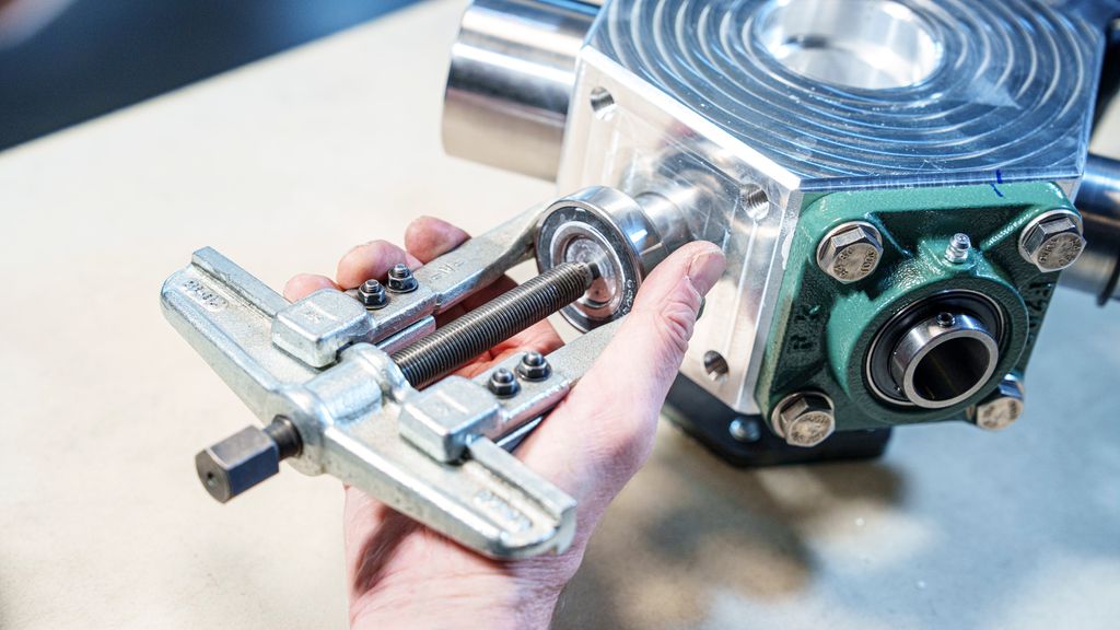 Ei hånd som holder et verktøy med to bein festa til et lager. Foto.