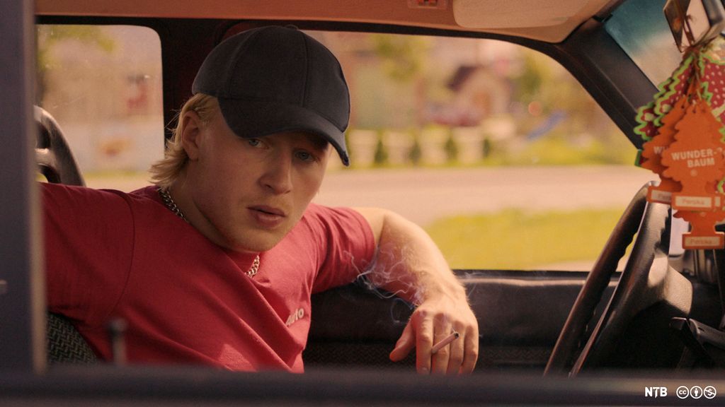 Ung mann med caps og tent sigarett i en bil. Foto.