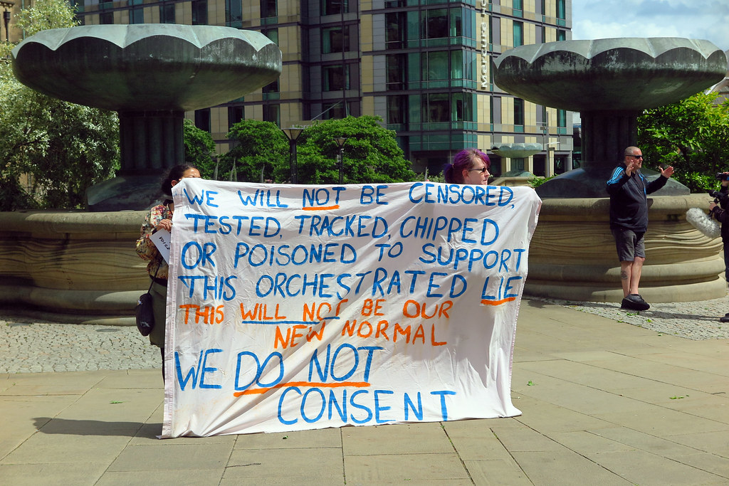 Vaksinemotstandarar held opp eit banner der dei gir uttrykk for konspirasjonsteoriar og sterk motstand mot covid-19-vaksinasjonen. Foto.