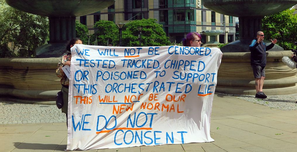 Vaksinemotstandarar held opp eit banner der dei gir uttrykk for konspirasjonsteoriar og sterk motstand mot covid-19-vaksinasjonen. Foto.
