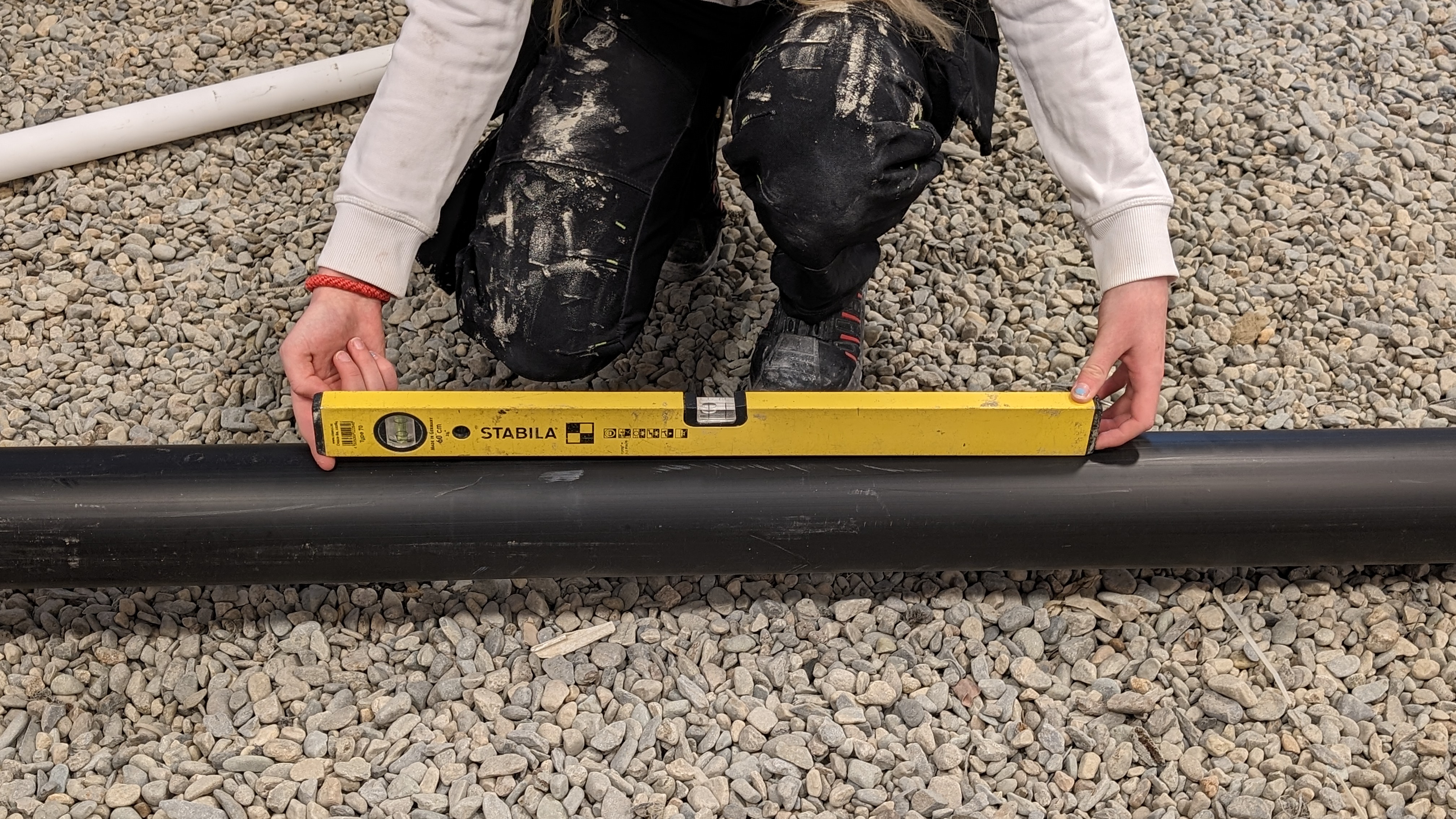 En person har lagt et vater ned på et avløpsrør og har lagt pekefingeren imellom vateret og røret i den lave enden av vateret. Foto.